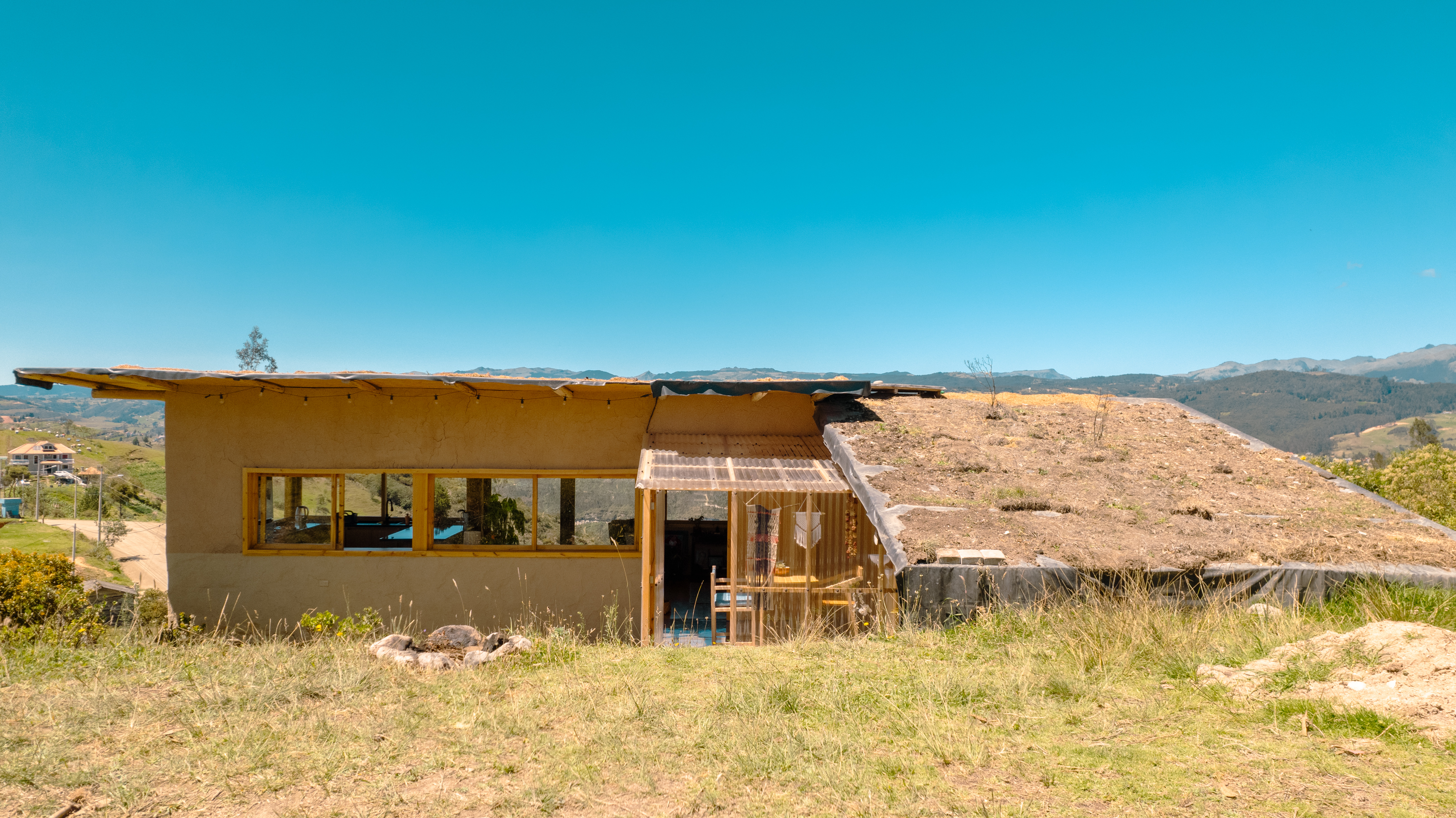 Casa Bhumi — la cubierta verde viva que se funde con la loma, junto a la galería de policarbonato