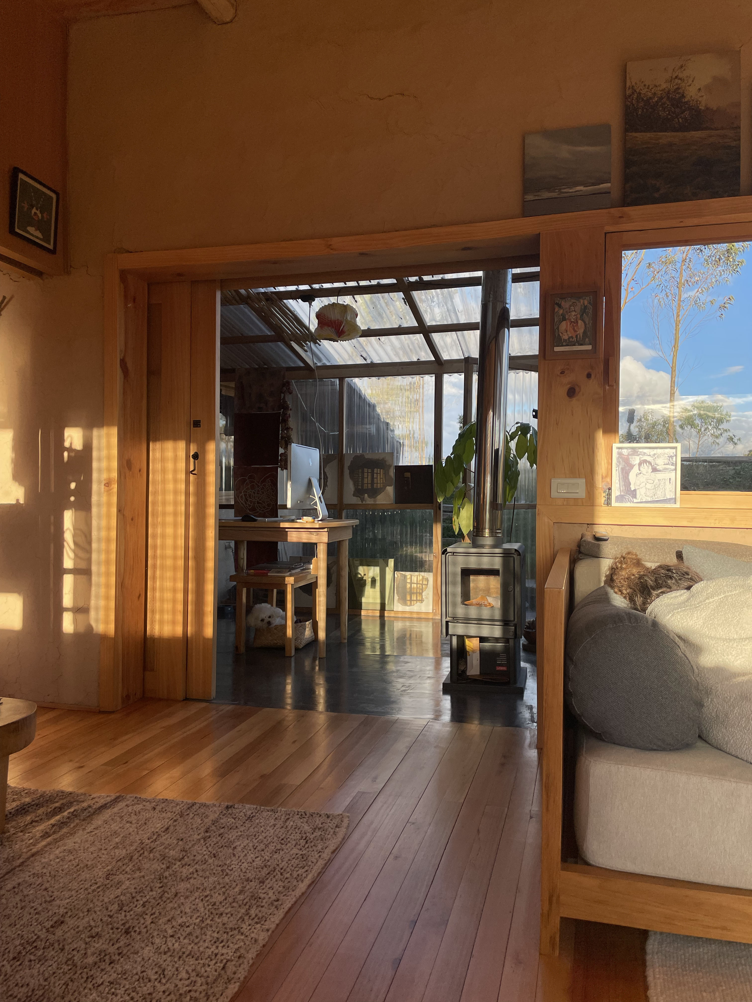 Casa Bhumi — galería de policarbonato con estufa de leña y escritorio, muros de tierra revocada en tono ocre