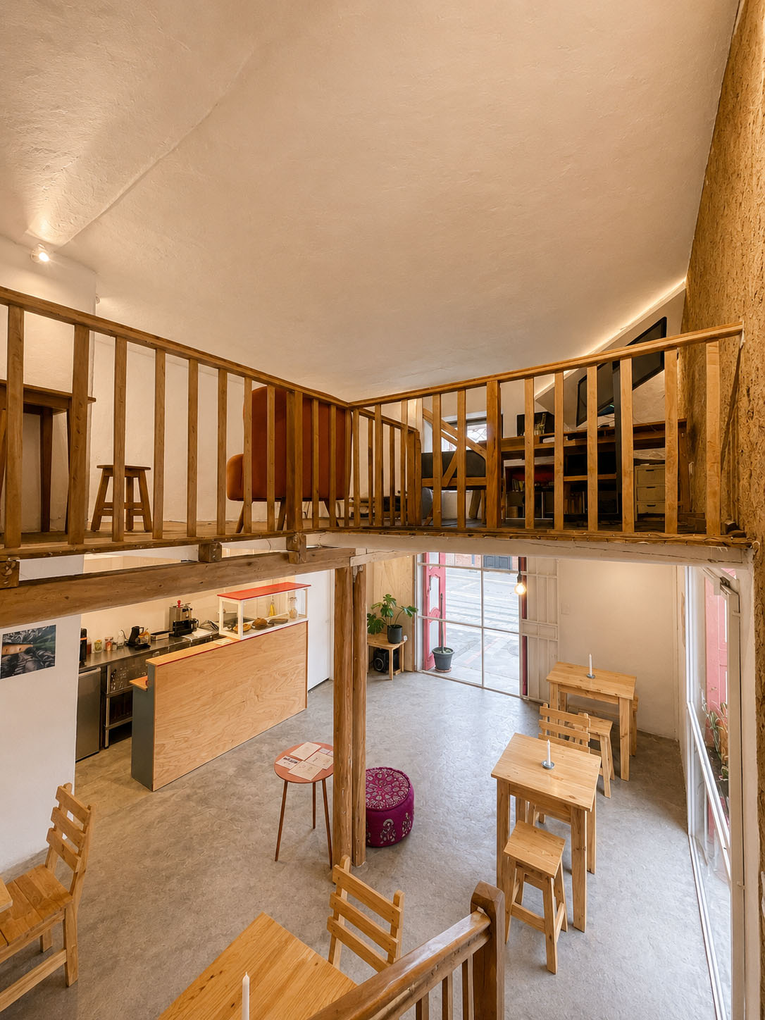 Café-Estudio — vista cenital del vacío de la escalera de madera entre los muros de tapial, mirando hacia el café en la planta baja