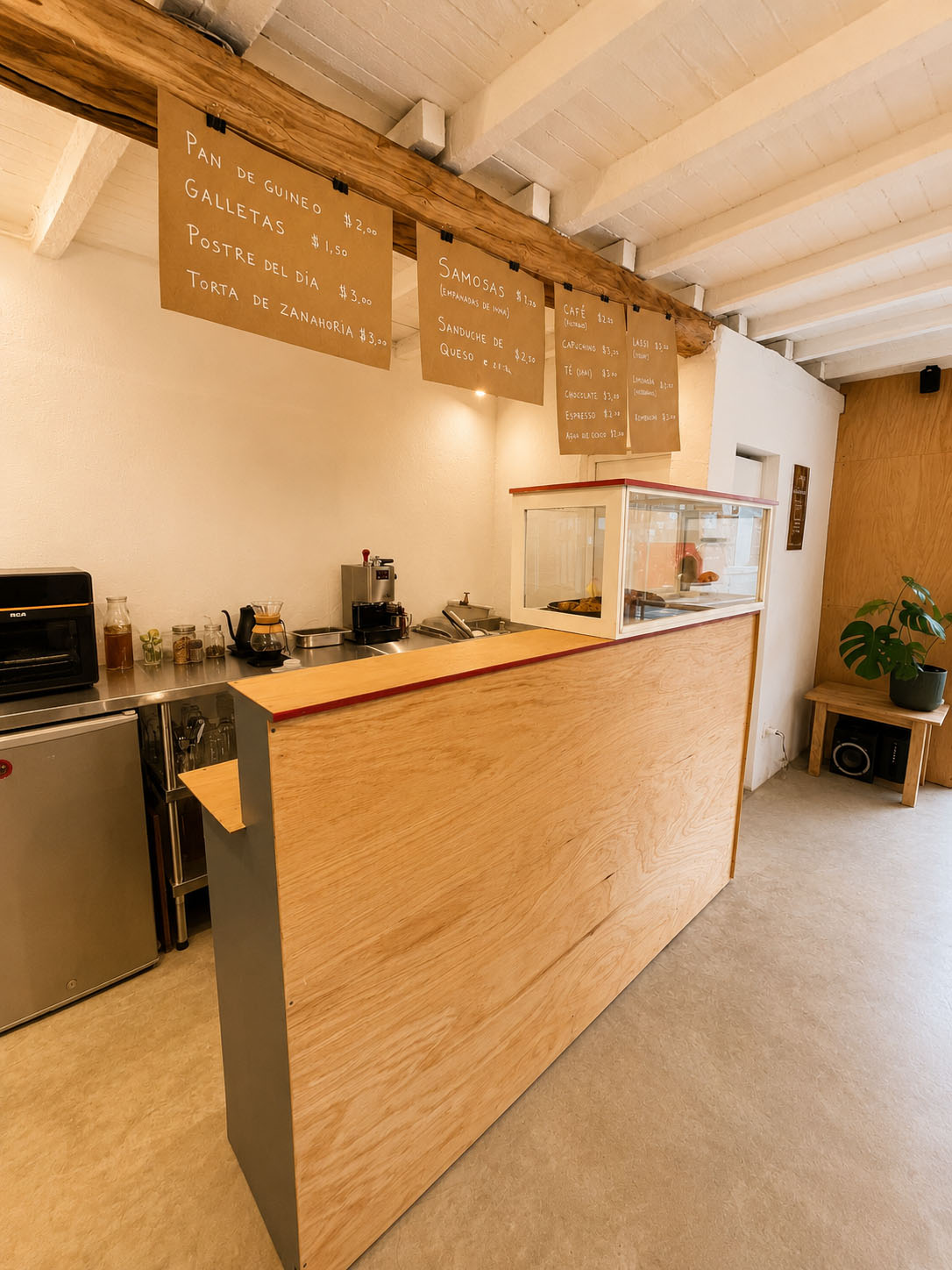 Café-Estudio — muro lateral con un mural de árbol, manos y casitas pintado por artistas invitados, junto a la puerta roja y macetas con plantas