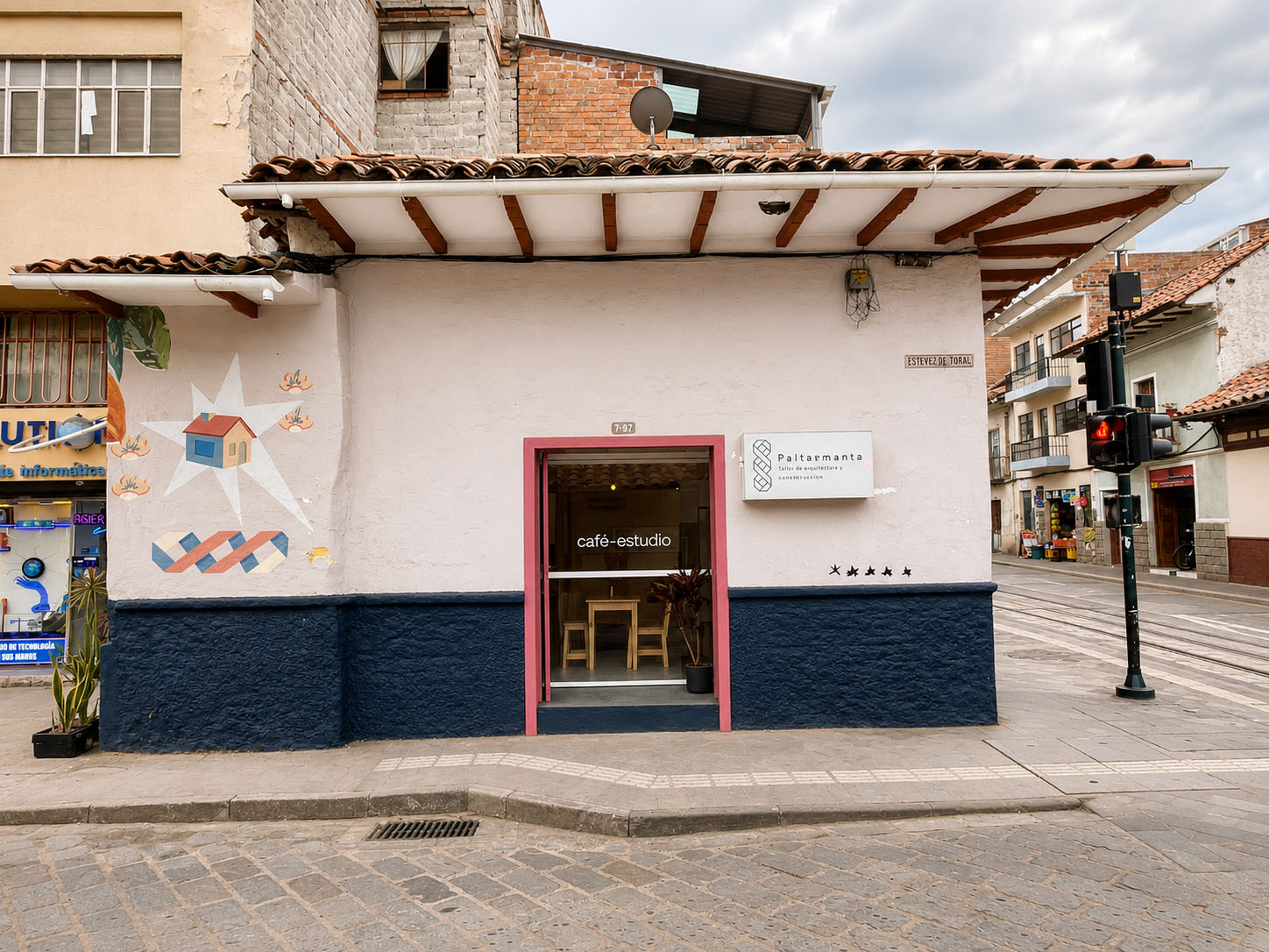 Café-Estudio — salón de la cafetería con barra de contrachapado, columna y vigas de madera, piso de cemento pulido y la escalera al fondo contra el muro de tapial
