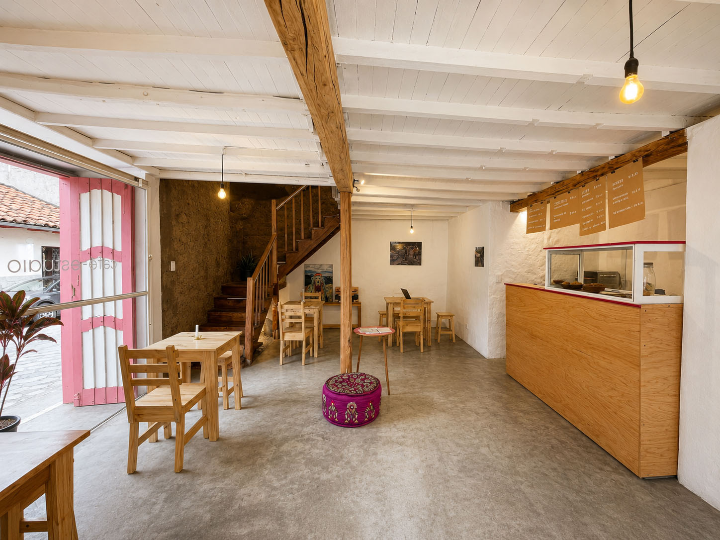 Café-Estudio — mesa de pino junto a la escalera de madera, con el muro de bahareque visto y un jardín de piedras al pie de la grada