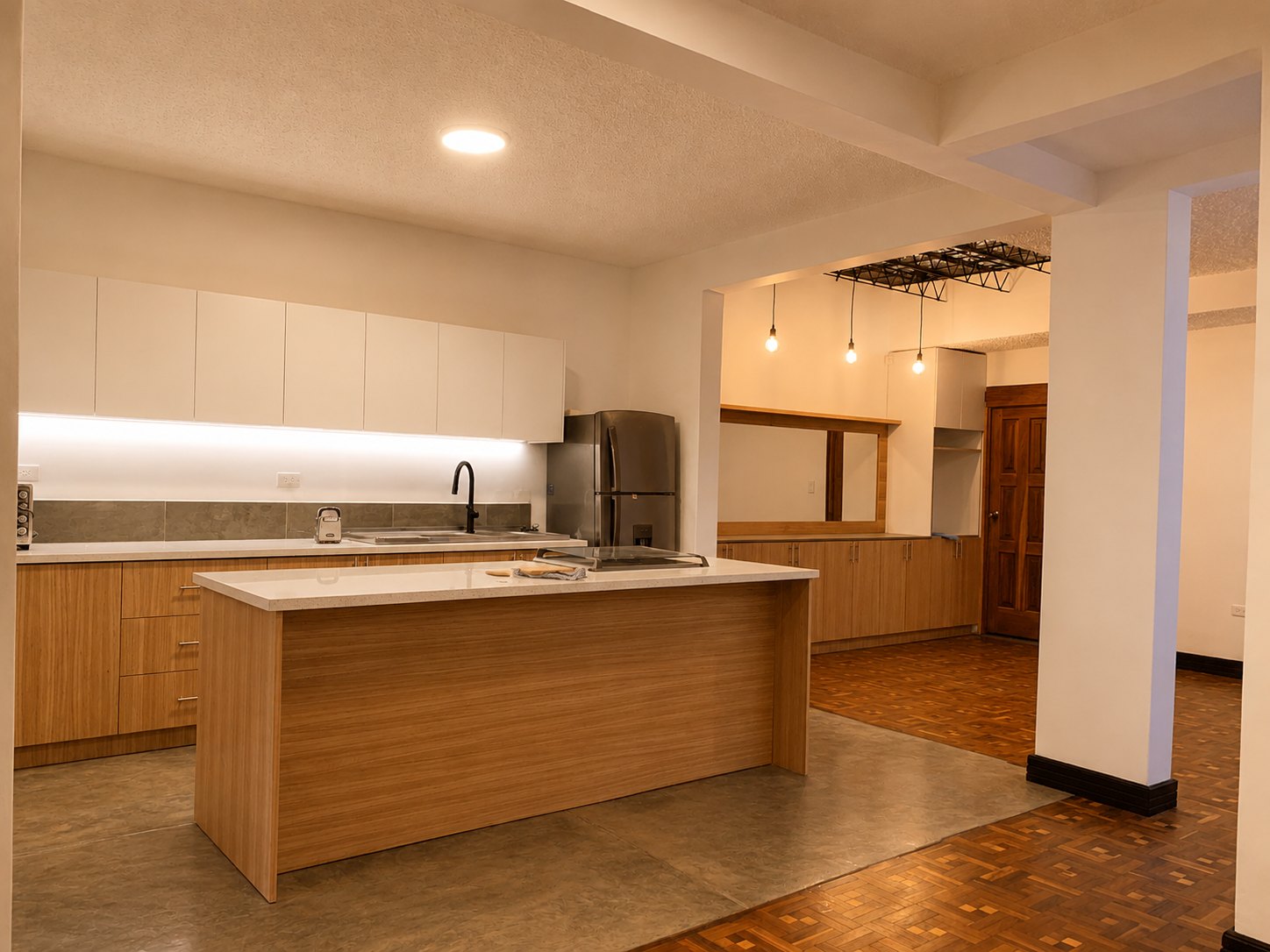Departamento Vane y David — vista amplia de la cocina abierta hacia el comedor, transición entre concreto pulido y parquet recuperado, puerta de madera original