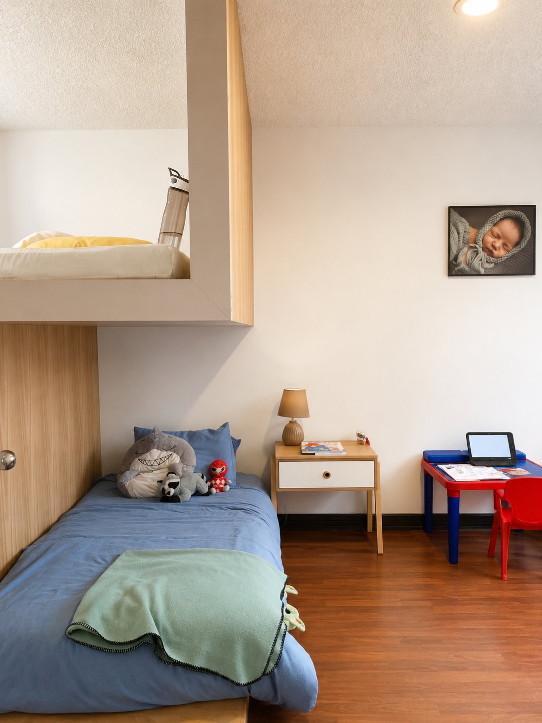 Departamento Vane y David — dormitorio de niños visto a lo largo, peluches sobre la cama, lámpara de mesa y mesa de trabajo infantil roja y azul