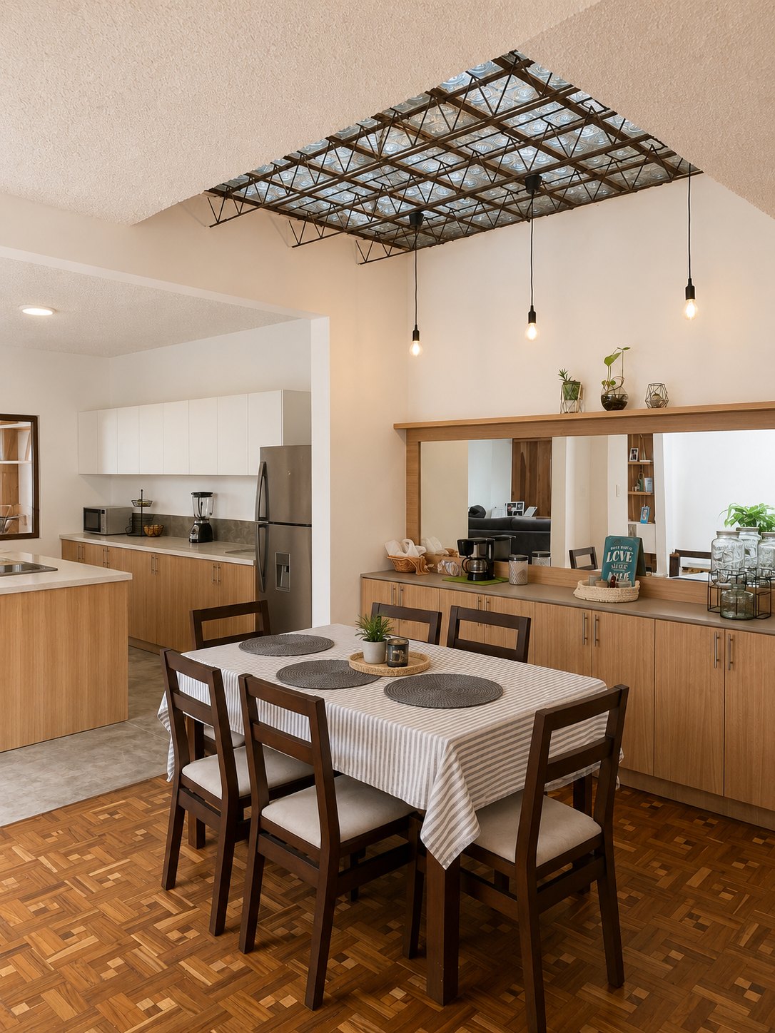 Departamento Vane y David — comedor con mesa de madera oscura bajo el tragaluz de botellas recuperadas, cocina al fondo