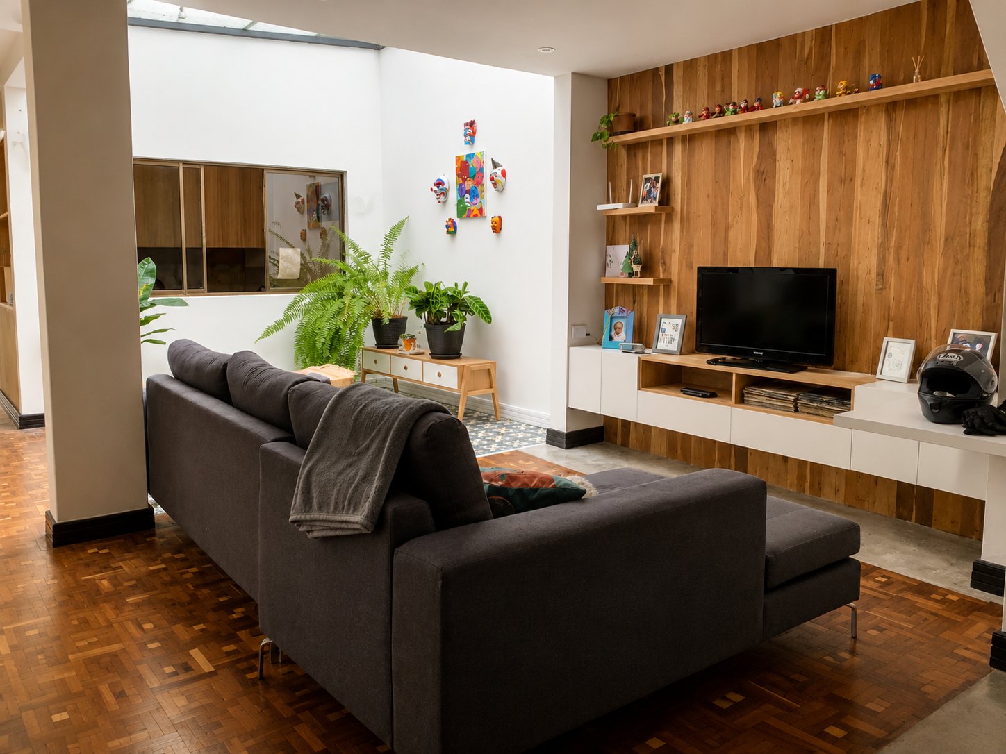 Departamento Vane y David — sala con sofá seccional gris, muro revestido en tablones de madera con repisas y televisor, piso de parquet recuperado y concreto pulido