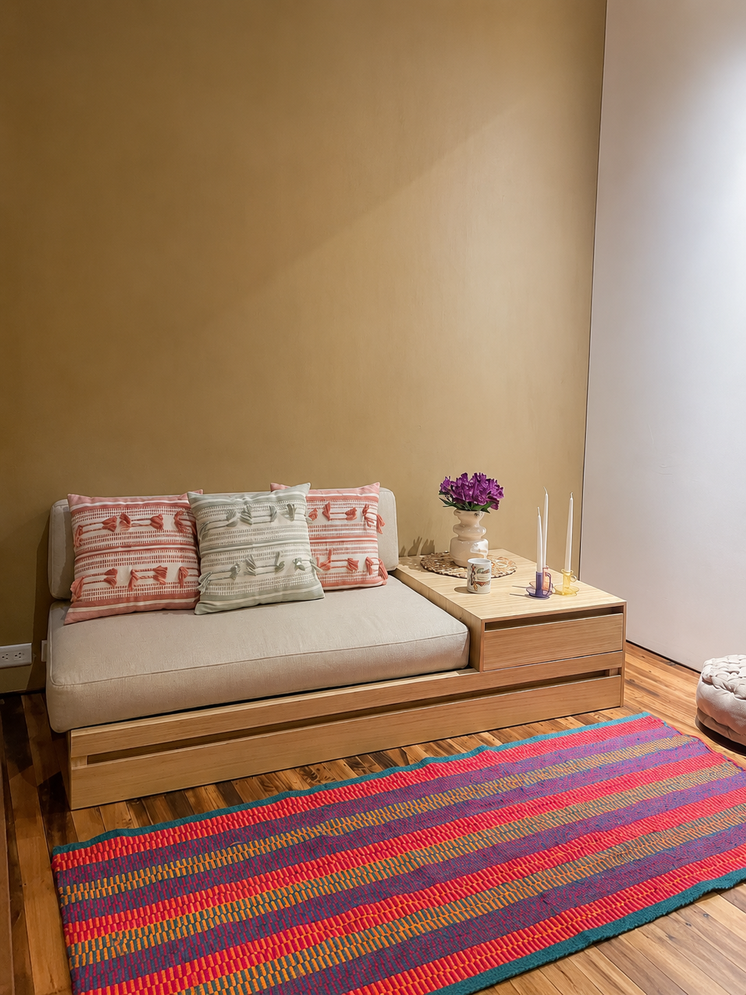 Diván modular bajo de madera con colchón corrido y mesa lateral con cajón, sobre un tapiz de rayas de colores