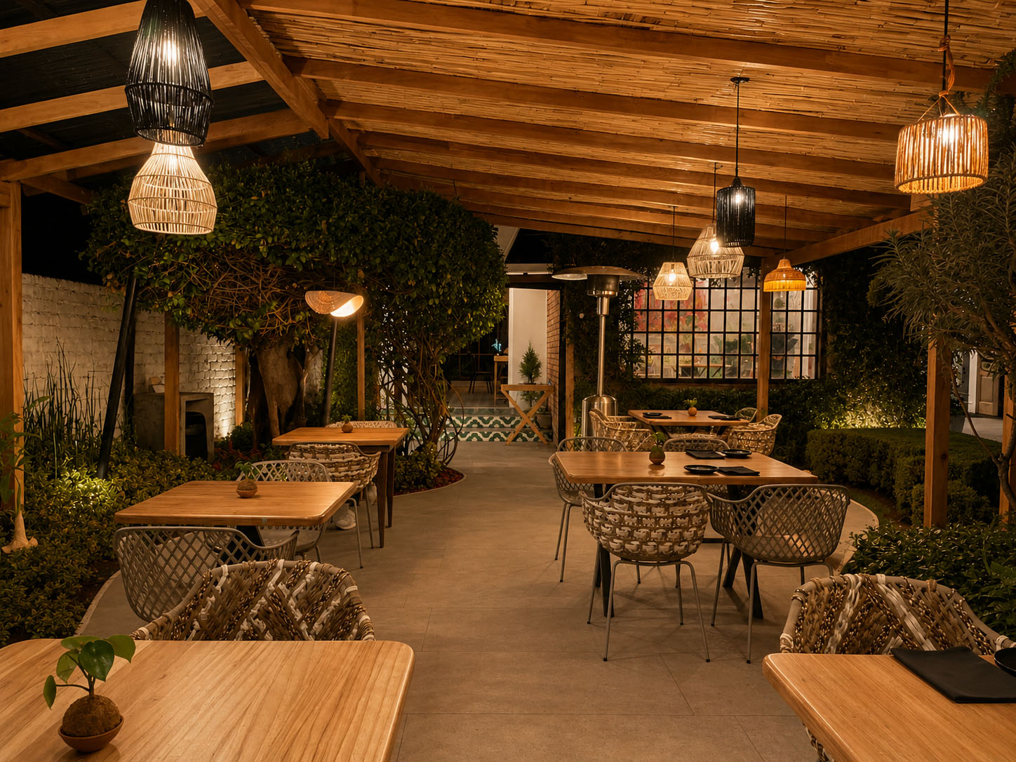 Dos Sucres — terraza bajo pérgola de madera iluminada de noche, con lámparas tejidas, vegetación y sillas de artesanía