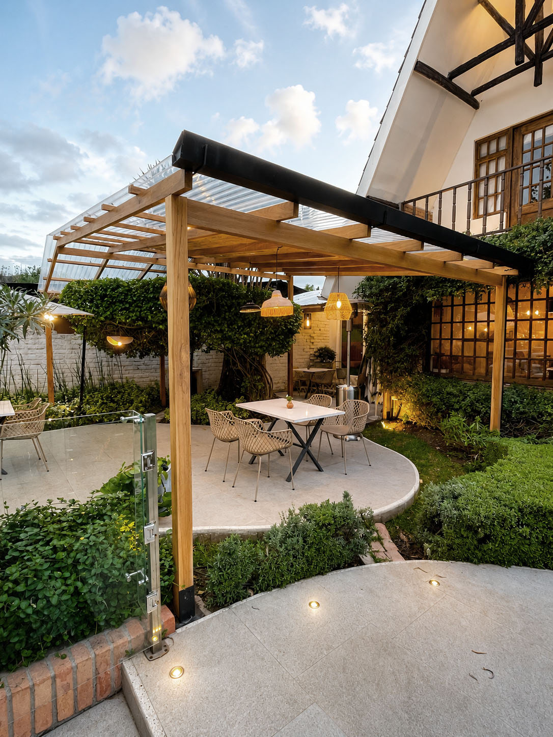 Dos Sucres — terraza bajo pérgola de madera al atardecer, con sillas tejidas por artesanos y jardín