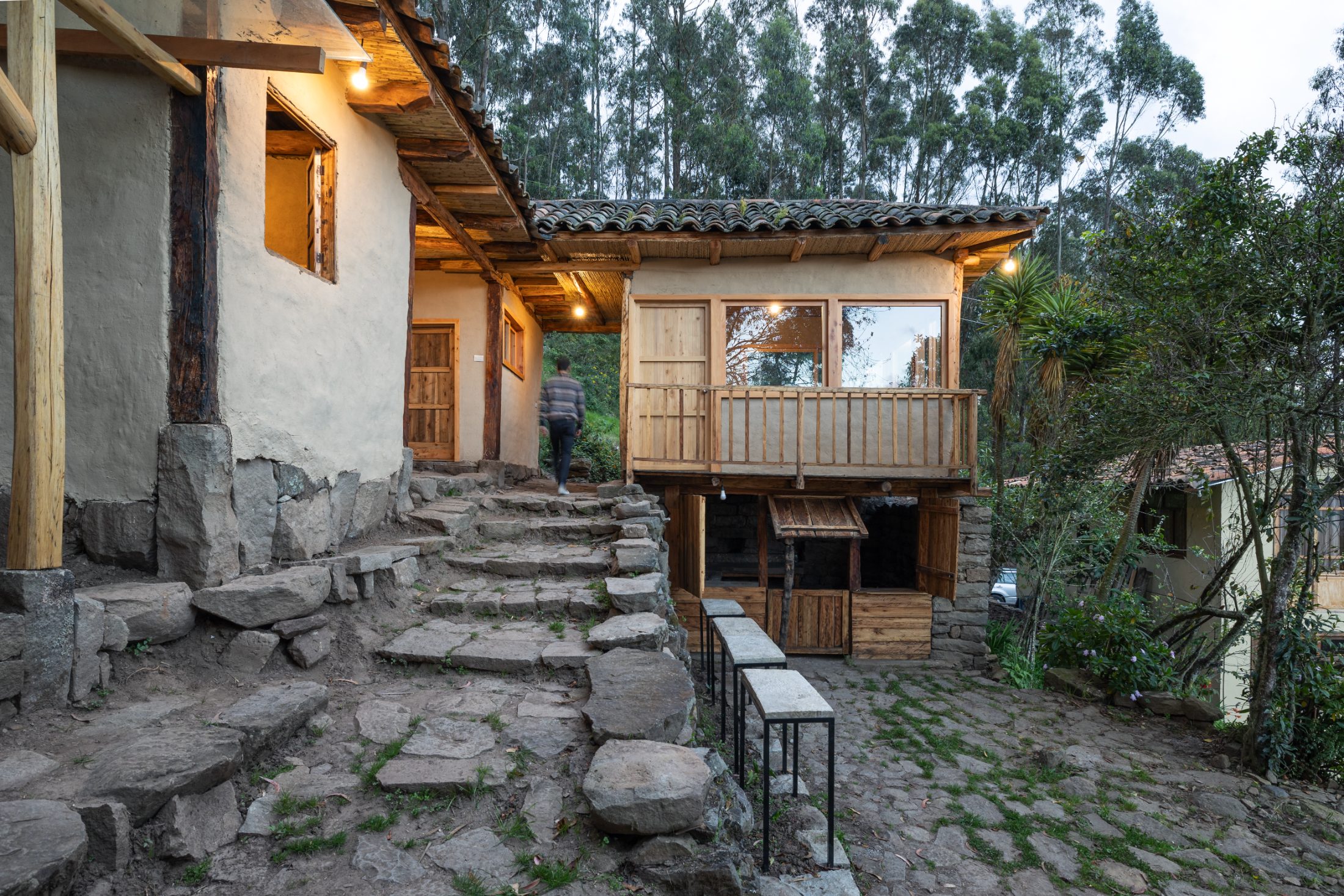 KANTUTA — acceso por escalera de piedra y casa de adobe restaurada al anochecer, anexo con balcón de madera y fogón exterior