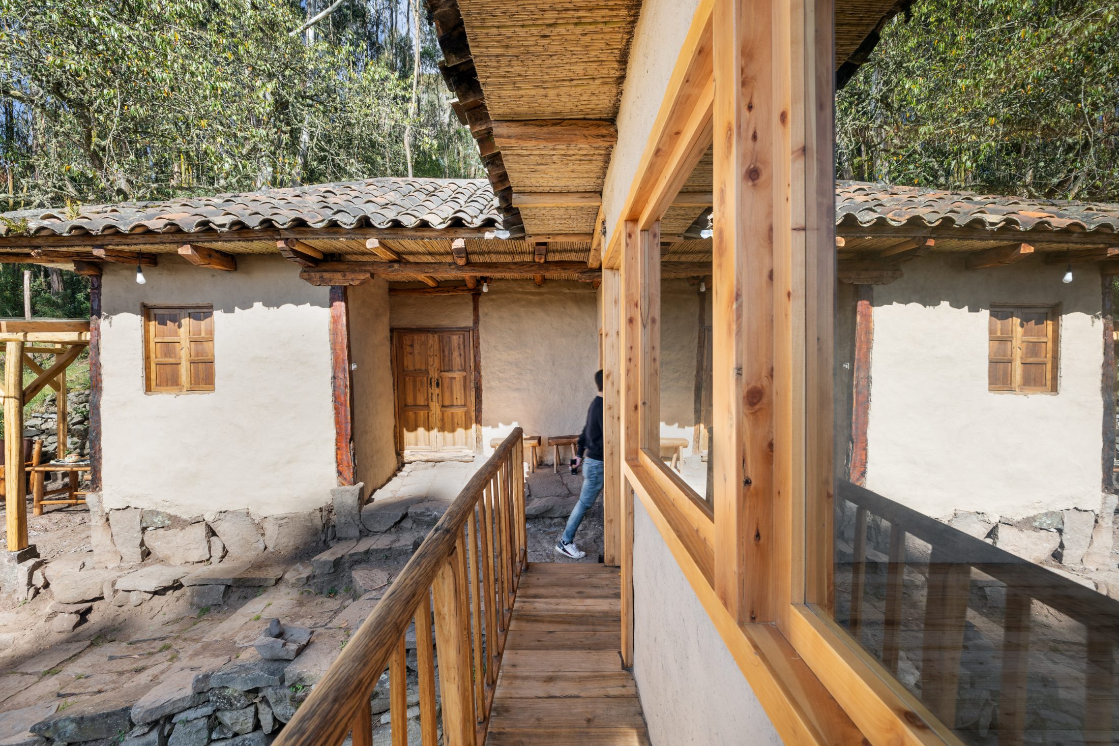 Pasarela de madera entre el anexo nuevo y la vivienda restaurada, muros de tapial blanqueado