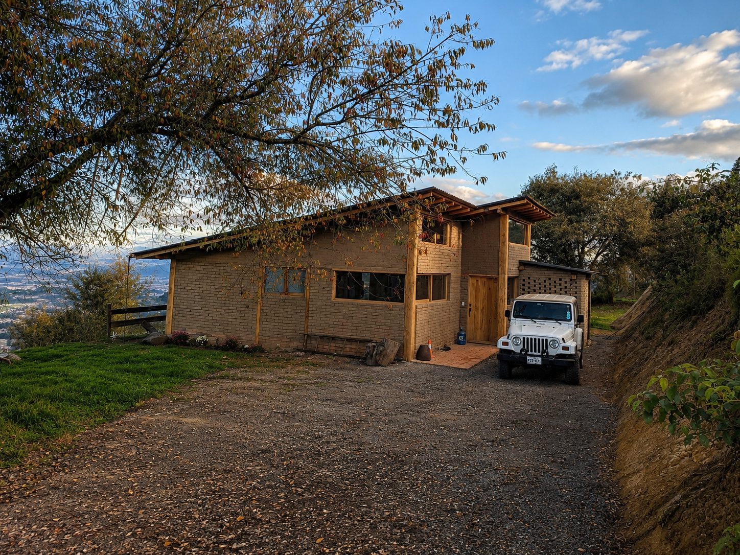 Casa de Ladrillo Pre-cocido — fachada de acceso a la hora dorada, jeep estacionado bajo el alero