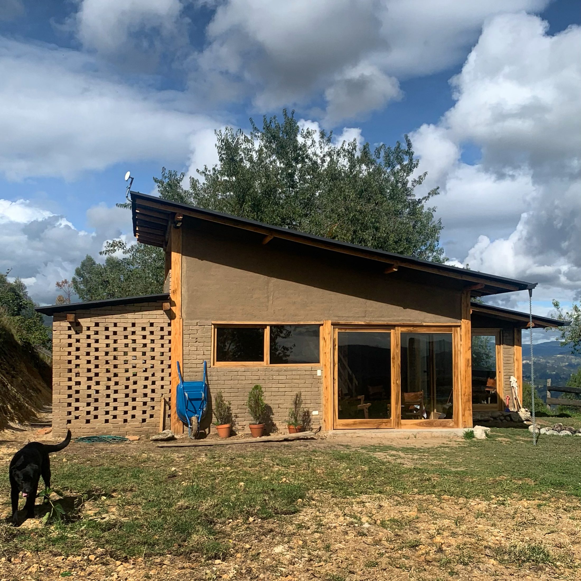 Casa de Ladrillo Pre-cocido — fachada lateral con celosía de ladrillo crudo y ventanal hacia el valle, perro labrador en primer plano