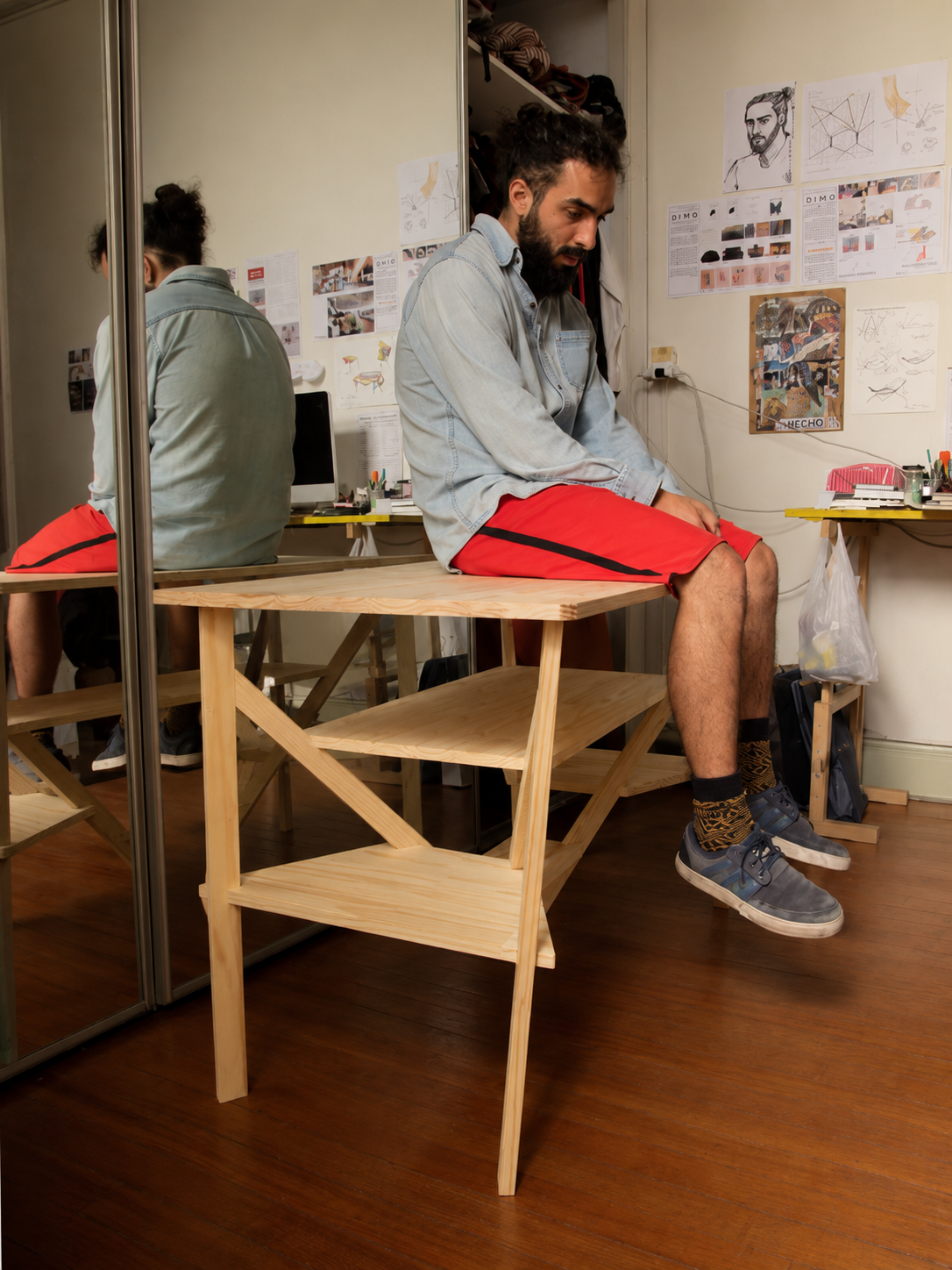 El diseñador sentado sobre su primera mesa de madera, en el taller del posgrado, probando si la estructura resistía su peso