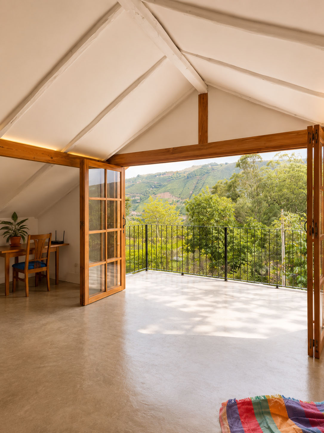 Casa de Tapial, después — puertas plegables de madera abiertas al balcón con baranda metálica y el valle verde al fondo