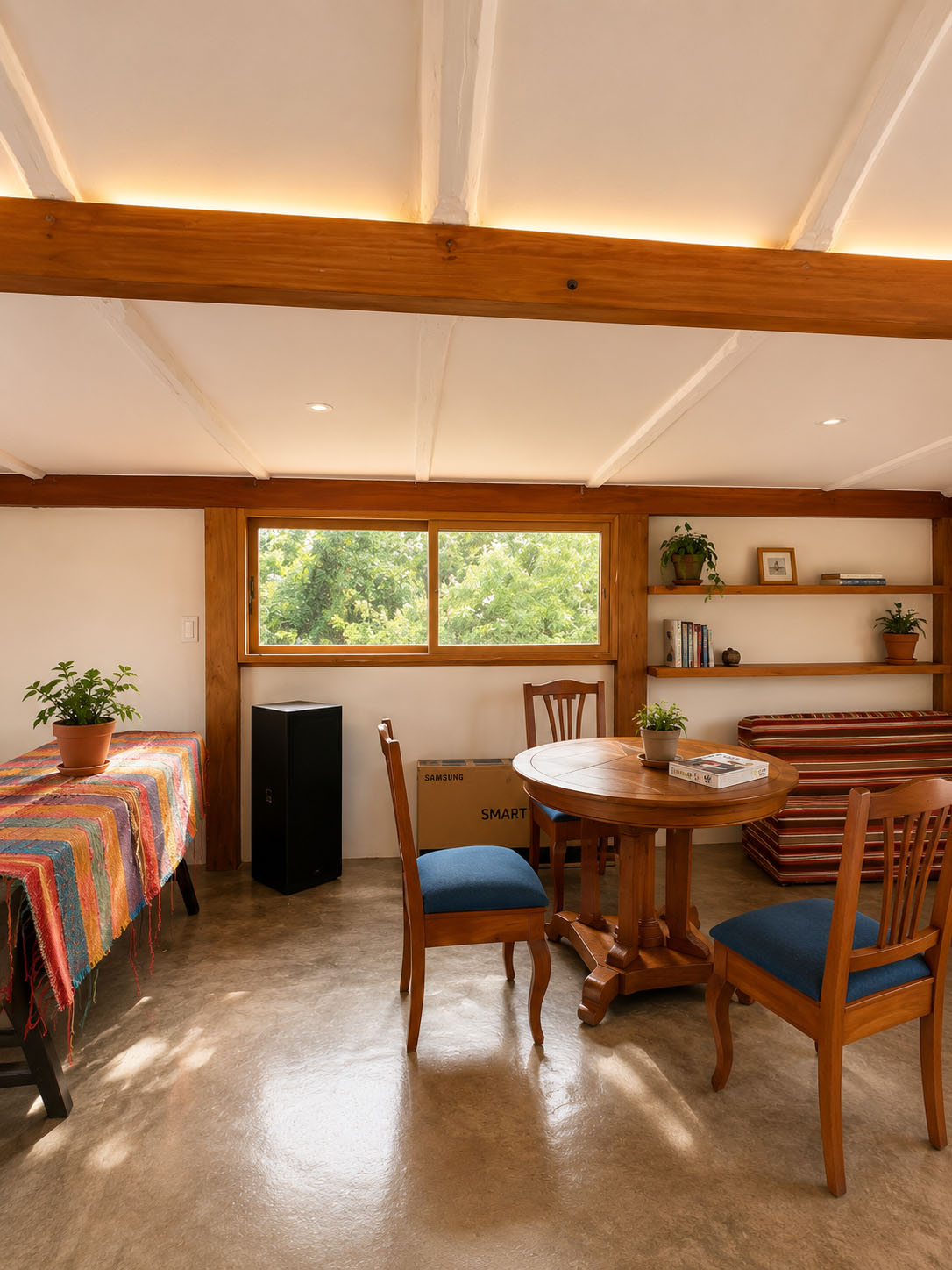 Casa de Tapial, después — mesa redonda con sillas azules, estantería de madera y cojines a rayas bajo la cubierta iluminada