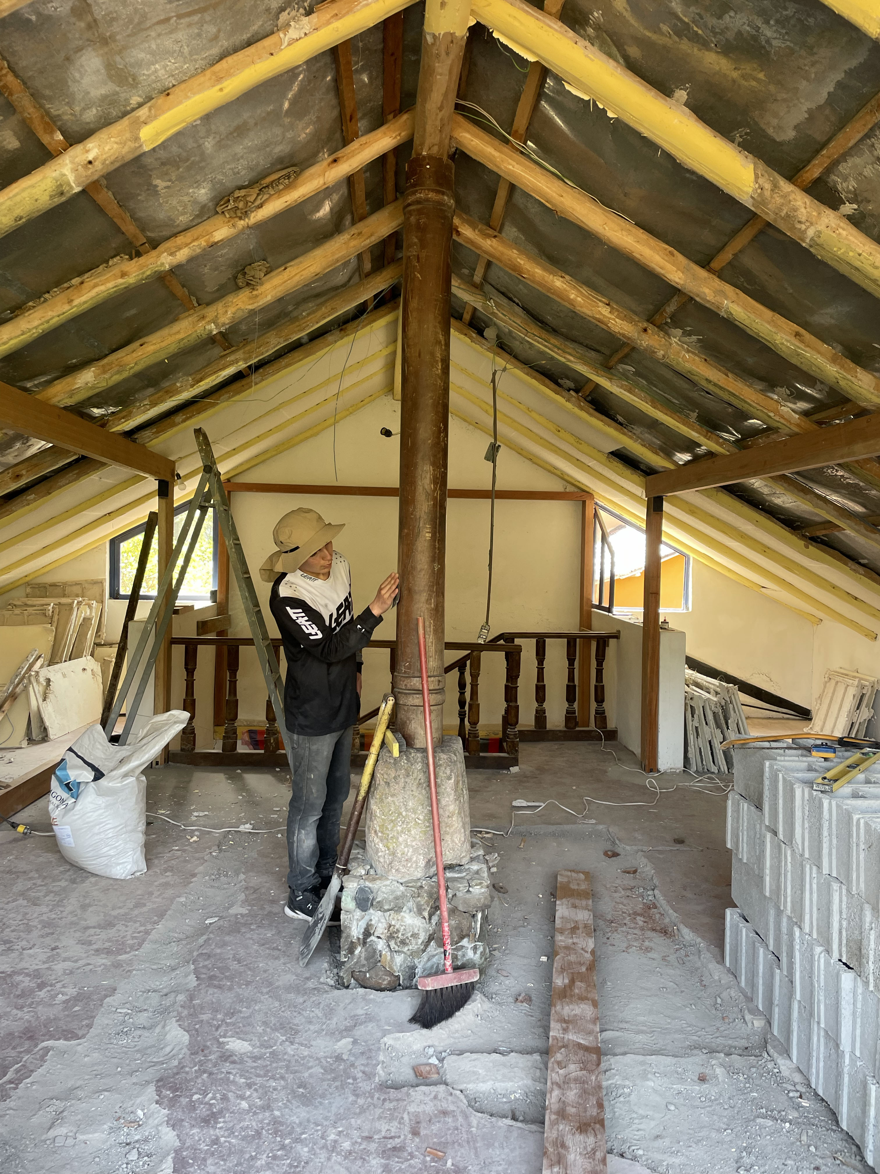 Casa de Tapial, proceso — un trabajador revisa la columna central de madera sobre su base de piedra, con la cubierta descubierta